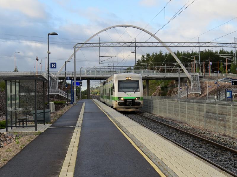 Henkilöjuna saapuu rautatiepysäkille, taustalla iso kaarimuoto.