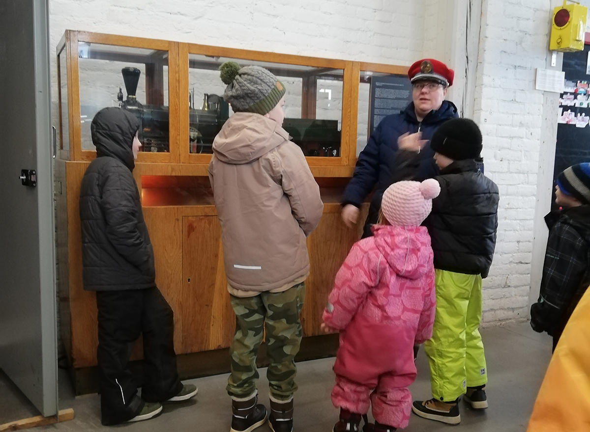 Lapsia oppaan kanssa katsomassa vitriinissä olevaa pienoismallihöyryveturia.