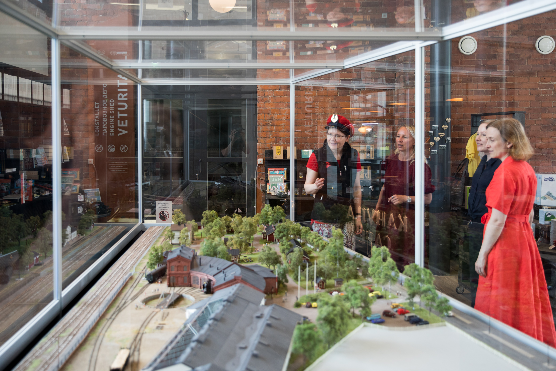 Opas kertoo kolmelle henkilölle museoalueesta Rautatiemuseon pienoismallin luona museon aulassa.