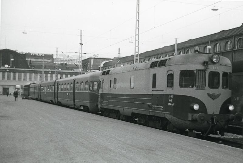 Henkilöjuna rautatieaseman laiturissa, taustalla rakennuksia.